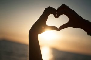 hand heart sign with sunset in background